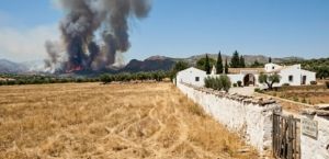 Dry vegetation near a white Spanish country house highlighting wildfire risk.