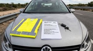 Chaleco reflectante y documento de asistencia en viaje sobre el capó de un coche.